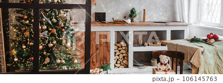 Home New Year's interior. Christmas tree with gifts, decorated with garlands in the kitchen. Cozy atmosphere of a home holiday, loft design of the room, Scandinavian style. Home New Year's interior. Christmas tree with gifts, decorated with garlands in the kitchen. Cozy atmosphere of a home holiday, loft design of the room, Scandinavian style. 106145763