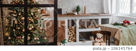 Home New Year's interior. Christmas tree with gifts, decorated with garlands in the kitchen. Cozy atmosphere of a home holiday, loft design of the room, Scandinavian style. Home New Year's interior. Christmas tree with gifts, decorated with garlands in the kitchen. Cozy atmosphere of a home holiday, loft design of the room, Scandinavian style. 106145764