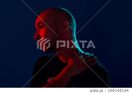Studio shot of a young tattoed bald man posing against a blue background. 90s style. Studio shot of a young tattoed bald man posing against a blue background. 90s style. 106148184
