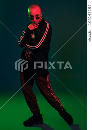 Studio shot of a young tattoed bald man posing against a colorful background. 90s style. Studio shot of a young tattoed bald man posing against a colorful background. 90s style. 106148190