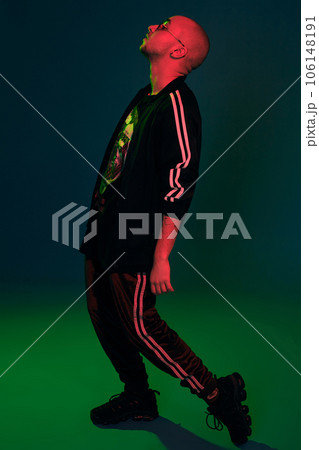 Studio shot of a young tattoed bald man posing against a colorful background. 90s style. Studio shot of a young tattoed bald man posing against a colorful background. 90s style. 106148191