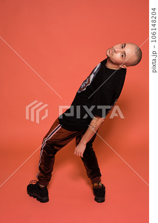 Studio shot of a young tattoed bald man posing against a pink background. 90s style. 106148204