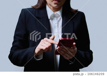 Closeup of business woman's hands using smartphone, on gray background Closeup of business woman's hands using smartphone, on gray background 106148209