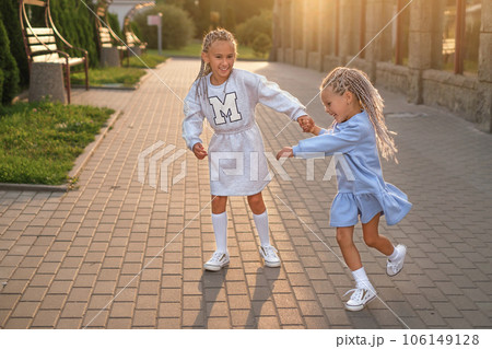Two little sisters are happily spinning on the city streets at sunset. Funny girls laugh holding hands. Two little sisters are happily spinning on the city streets at sunset. Funny girls laugh holding hands. 106149128