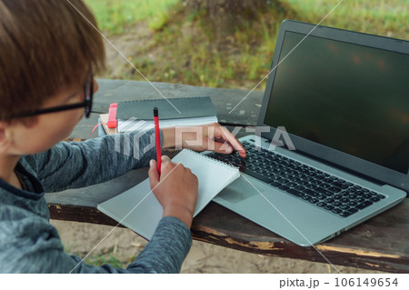 Smart student with glasses sitting at table where textbooks lying, holding pencil in hand and studying with laptop. Smart student with glasses sitting at table where textbooks lying, holding pencil in hand and studying with laptop. 106149654