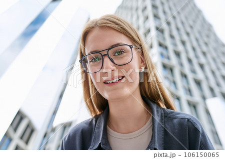 Teenage female in glasses looking at camera, glass skyscrapers background Teenage female in glasses looking at camera, glass skyscrapers background 106150065