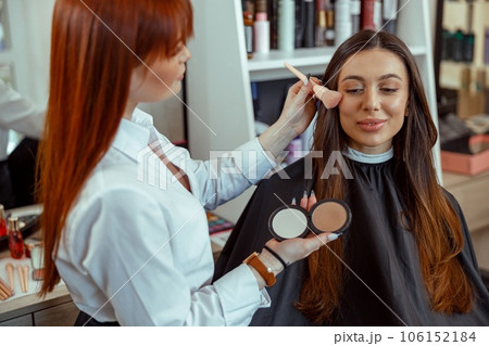 Professional makeup artist applying bronzer powder with a brush in beauty salon 106152184