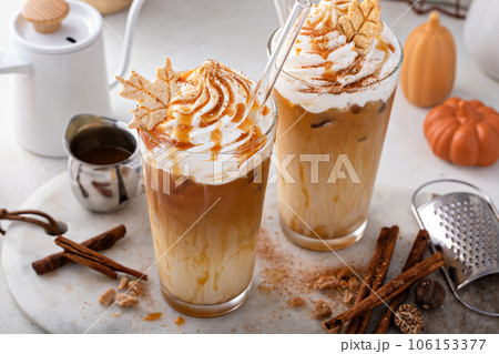 Iced pumpkin spice latte in tall glasses topped with whipped cream 106153377