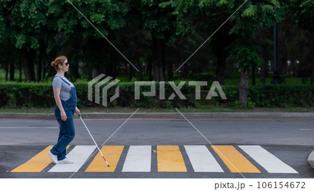 Blind pregnant woman crosses the road at a crosswalk with a cane.  106154672
