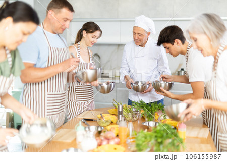 Smiling old man chef of cooking course teaching attendees how to mix sauce Smiling old man chef of cooking course teaching attendees how to mix sauce 106155987