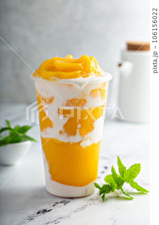 Coconut cream and mango layered smoothie in a tall glass Coconut cream and mango layered smoothie in a tall glass 106156022