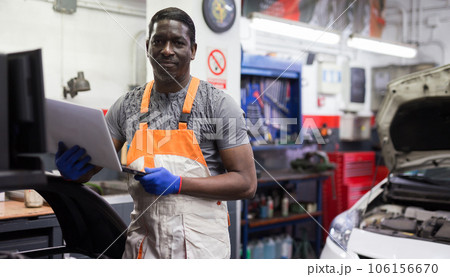 African mechanic man using a laptop computer checking car in workshop 106156670