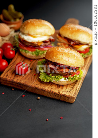 Close-up of a delicious fresh homemade burger with lettuce, cheese, onion and tomato on a rustic wooden board on a dark background 106162581