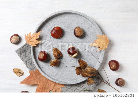 Brown chestnut fruits with yellow leaves in a gray bowl Brown chestnut fruits with yellow leaves in a gray bowl 106162801