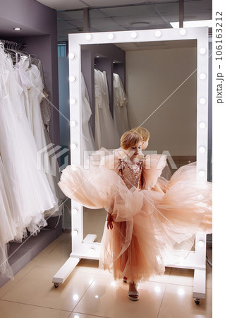 A little girl in a boutique chooses a dress in front of a mirror. 106163212