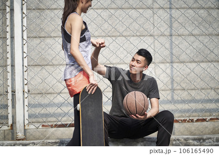 young asian adult male basketball player and female skateboarder bumping fists on a outdoor court 106165490