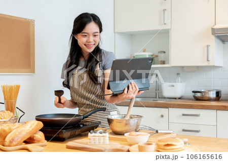 A happy Asian woman is reading an online recipe on her tablet and enjoying making pancakes 106165616