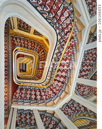 Abstract shape luxurious stairs with red carpet cover and golden handrail. Hypnotic pattern swirl staircase with mirror reflections on the stairwell walls Abstract shape luxurious stairs with red carpet cover and golden handrail. Hypnotic pattern swirl staircase with mirror reflections on the stairwell walls 106166853