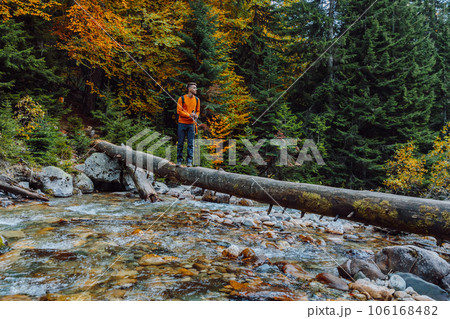 Hiker man staying on a log over the mountain river in autumnal forest. 106168482