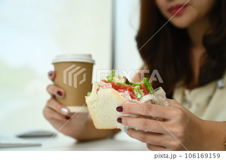 Woman hands holding delicious sandwich and paper cup coffee. Fast food and lifestyle concept Woman hands holding delicious sandwich and paper cup coffee. Fast food and lifestyle concept 106169159