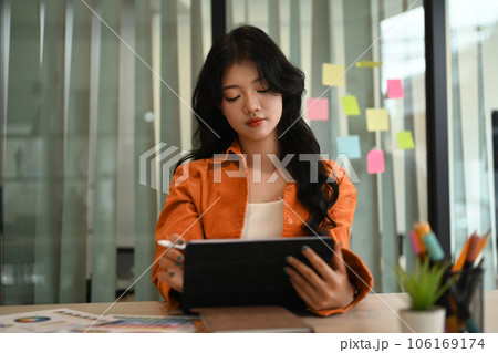 Pretty Asian female graphic designer drawing something on digital tablet working on new design project at creative office 106169174