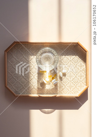 Water glass and different vitamin capsules on tray in morning light. Water glass and different vitamin capsules on tray in morning light. 106170652