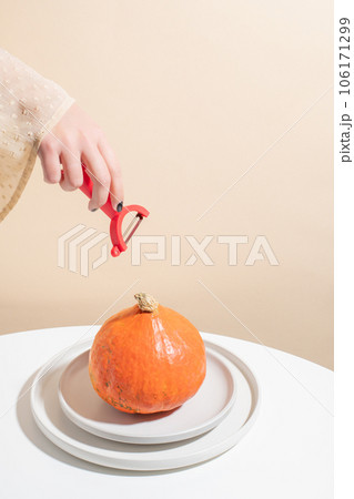 Still-life. The girl reaches out with a cleaning knife to a whole pumpkin. Beige background . Concept. 106171299
