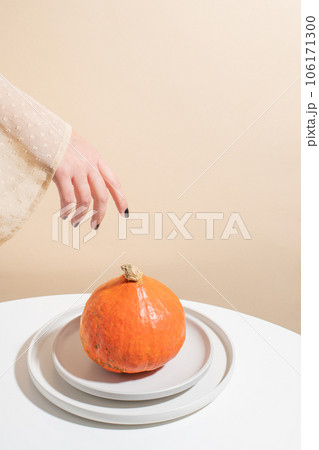 Still-life. The girl reaches out with her hand to the whole pumpkin. Beige background . Concept. Still-life. The girl reaches out with her hand to the whole pumpkin. Beige background . Concept. 106171300