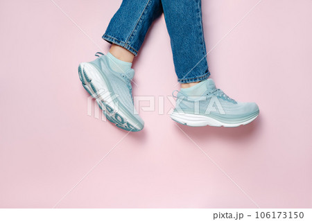 Women legs in blue jeans and new green blue modern running shoes on pink background. Stylish monochrome shoes for active people that incorporate new health technology. Top view Women legs in blue jeans and new green blue modern running shoes on pink background. Stylish monochrome shoes for active people that incorporate new health technology. Top view 106173150