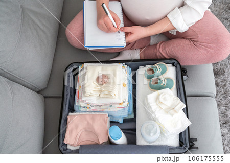 Pregnant woman at home, focused on writing a list, diligently packing suitcase for maternity hospital, embracing the future mother concept Pregnant woman at home, focused on writing a list, diligently packing suitcase for maternity hospital, embracing the future mother concept 106175555