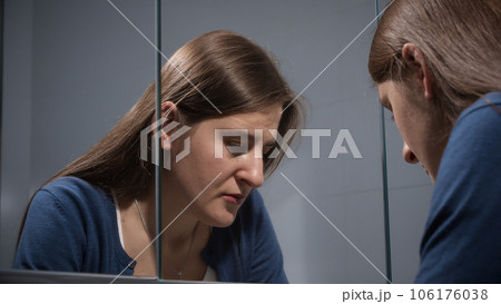 Upset stressed woman sighs at bathroom and looks in her reflection in mirror. Concept of depression, stress, mental illness and problems, loneliness and frustration. 106176038
