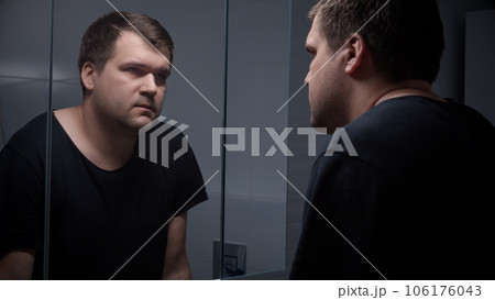 Young concentrated man feeling emotional pressure looking in his reflection in mirror Young concentrated man feeling emotional pressure looking in his reflection in mirror 106176043