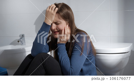 Crying woman suffering from depression sitting on floor in bathroom at home. Concept of depression, suicide, stress, mental illness, loneliness and frustration. Crying woman suffering from depression sitting on floor in bathroom at home. Concept of depression, suicide, stress, mental illness, loneliness and frustration. 106176077