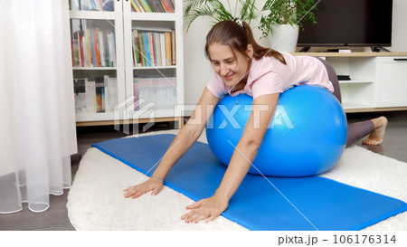 Smiling brunette woman doing yoga and fitness with big blue ball at home 106176314