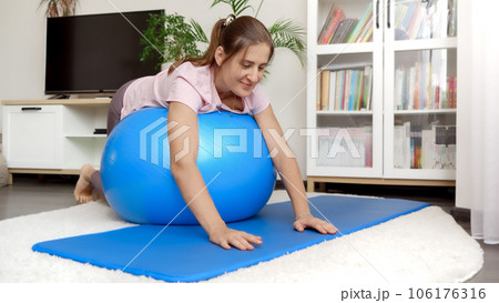 Smiling young woman lying on fitball and rolling over. Concept of healthcare, sports and yoga at home. 106176316