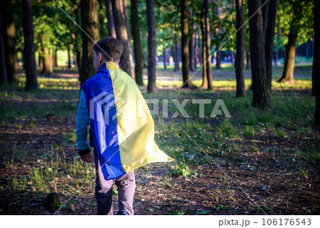 Worried teenager patriot wear blue yellow Ukrainian flag on his shoulders. Spring nature background. Ukraine national symbol. Patriotism 106176543