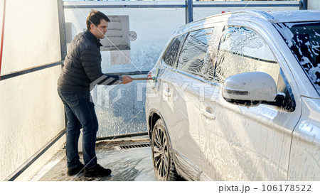 Young man washing his car at self-service carwash. Automobile care, transport cleaning, dirty car. Young man washing his car at self-service carwash. Automobile care, transport cleaning, dirty car. 106178522
