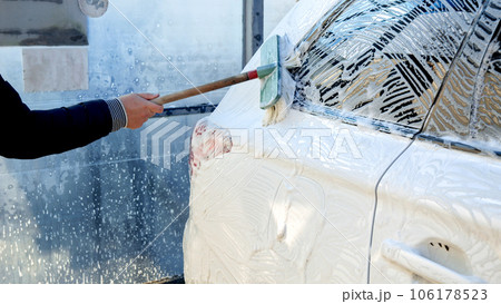 Closeup of man cleaning dirty white car with soft brush on self service car wash 106178523