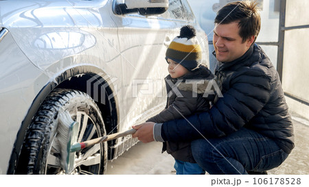 Little baby boy washing fathers' car with soap foam and brush at outdoor carwash. Automobile care, transport cleaning, dirty car. Little baby boy washing fathers' car with soap foam and brush at outdoor carwash. Automobile care, transport cleaning, dirty car. 106178528