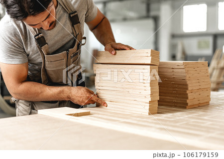 Young carpenter man looking and choosing wood plank at workshop in carpenter wood factory 106179159