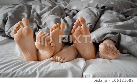 Closeup of parent's and child's feet showing from under the blanket on bed at morning. Concept of togetherness, happy childhood and parenting. Closeup of parent's and child's feet showing from under the blanket on bed at morning. Concept of togetherness, happy childhood and parenting. 106181088