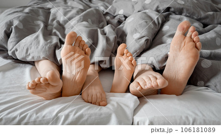 Parent's and child's feet happily tapping and wiggling under the blanket on a comfortable bed. Concept of family love, bonding, and playful moments shared at home. Parent's and child's feet happily tapping and wiggling under the blanket on a comfortable bed. Concept of family love, bonding, and playful moments shared at home. 106181089