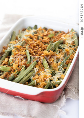 A traditional green bean casserole topped with French Fried Onions and cream of mushroom on white marble. Close up A traditional green bean casserole topped with French Fried Onions and cream of mushroom on white marble. Close up 106181264