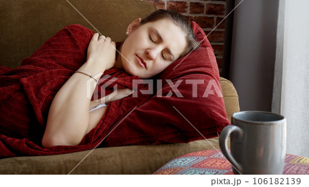 Young sick woman covering in plaid on sofa and coughing. Healthcare, female feeling sick at home, illness and health problems. 106182139