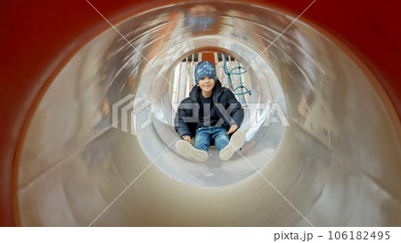 Little boy sliding down the tube slide on public playground. Happy kids, fun outdoors, leisure in park. 106182495
