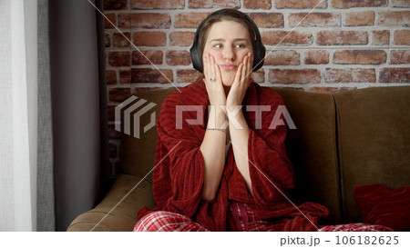 Portrait of thoughtful sad woman sitting on sofa and listening music in headphones. People relaxing at home, having fun, positive emotions and joy. 106182625