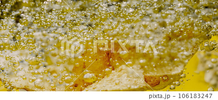 Deep fried potato chips under golden oil water. Frying rounded potatoes chip with hot boiling oil bubbles. Fast food and snack. Underwater cooking oily french fries or potatos chips in oils background 106183247