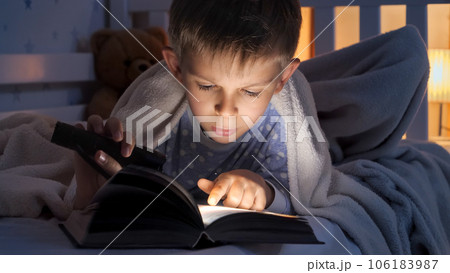 Portrait of boy with torch lying in bed and reading story book. Children education, development, secrecy, privacy, reading books. Portrait of boy with torch lying in bed and reading story book. Children education, development, secrecy, privacy, reading books. 106183987
