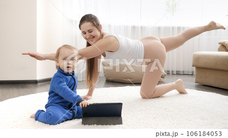 Happy smiling mother with babyy son doing fitness exercise and watching online training n tablet computer Happy smiling mother with babyy son doing fitness exercise and watching online training n tablet computer 106184053