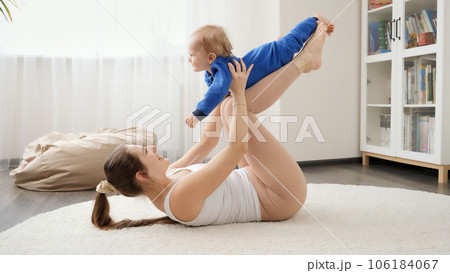Happy laughing baby boy having fun with mother doing fitness exercises on floor. Family healthcare, active lifestyle, parenting and child development Happy laughing baby boy having fun with mother doing fitness exercises on floor. Family healthcare, active lifestyle, parenting and child development 106184067
